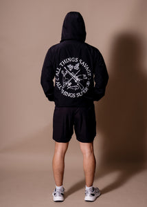 Person wearing a black hoodie with text and graphics on the back, standing against a brown background